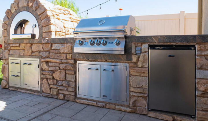 Outdoor kitchen island featuring a stainless steel Lion Premium Grill with, refrigerator, Built in Alfa Pizza oven and spacious countertop. The island showcases a sleek design with durable stone finishing, ideal for grilling and entertaining in any backyard setting.