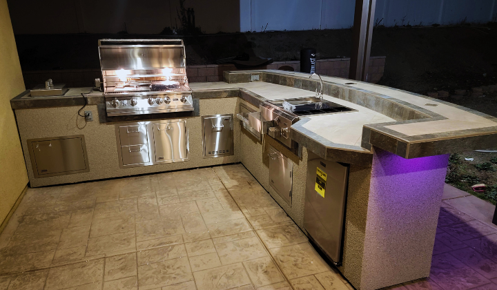 Outdoor kitchen island with Lion Gas Grill, side burners, refrigerator, and LED lights, providing a complete and stylish outdoor cooking station.