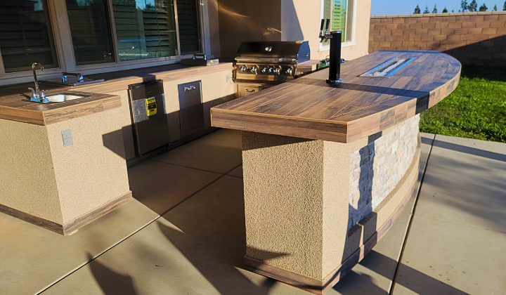 Outdoor kitchen island with a Lion Gas Grill, side burners, refrigerator, and integrated firepit, offering a cozy and functional outdoor cooking and entertainment area.