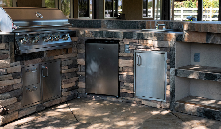 Outdoor kitchen island with a Lion Gas Grill, refrigerator, raised bar, and stackstone finish, creating a stylish and functional space for cooking and entertaining outdoors.