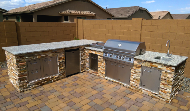 Outdoor kitchen island with a Lion Gas Grill, refrigerator, sink, seating, stackstone base, and LED lights for a stylish, functional outdoor space