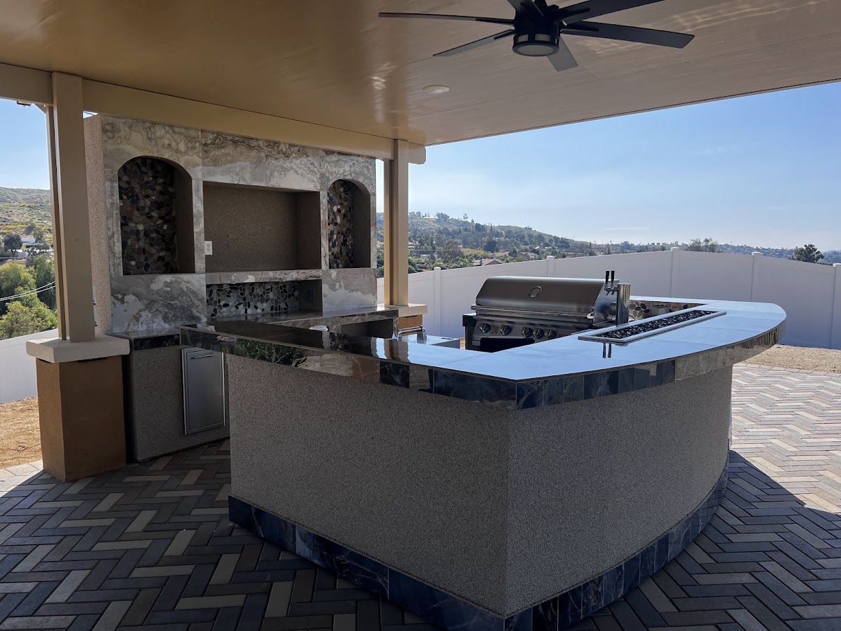 Full U-shaped outdoor kitchen with raised bar, integrated fire pit, and seating facing a custom TV wall in Riverside, CA