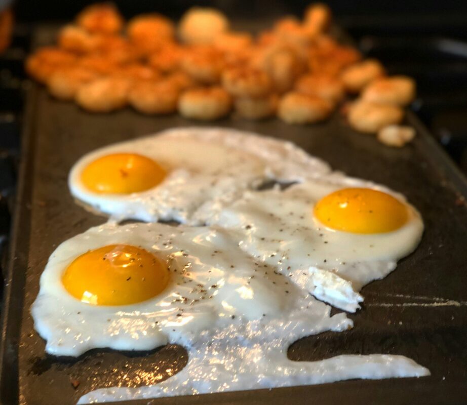 Bacon eggs and pancakes cooking on a Lion gas grill griddle for outdoor breakfast