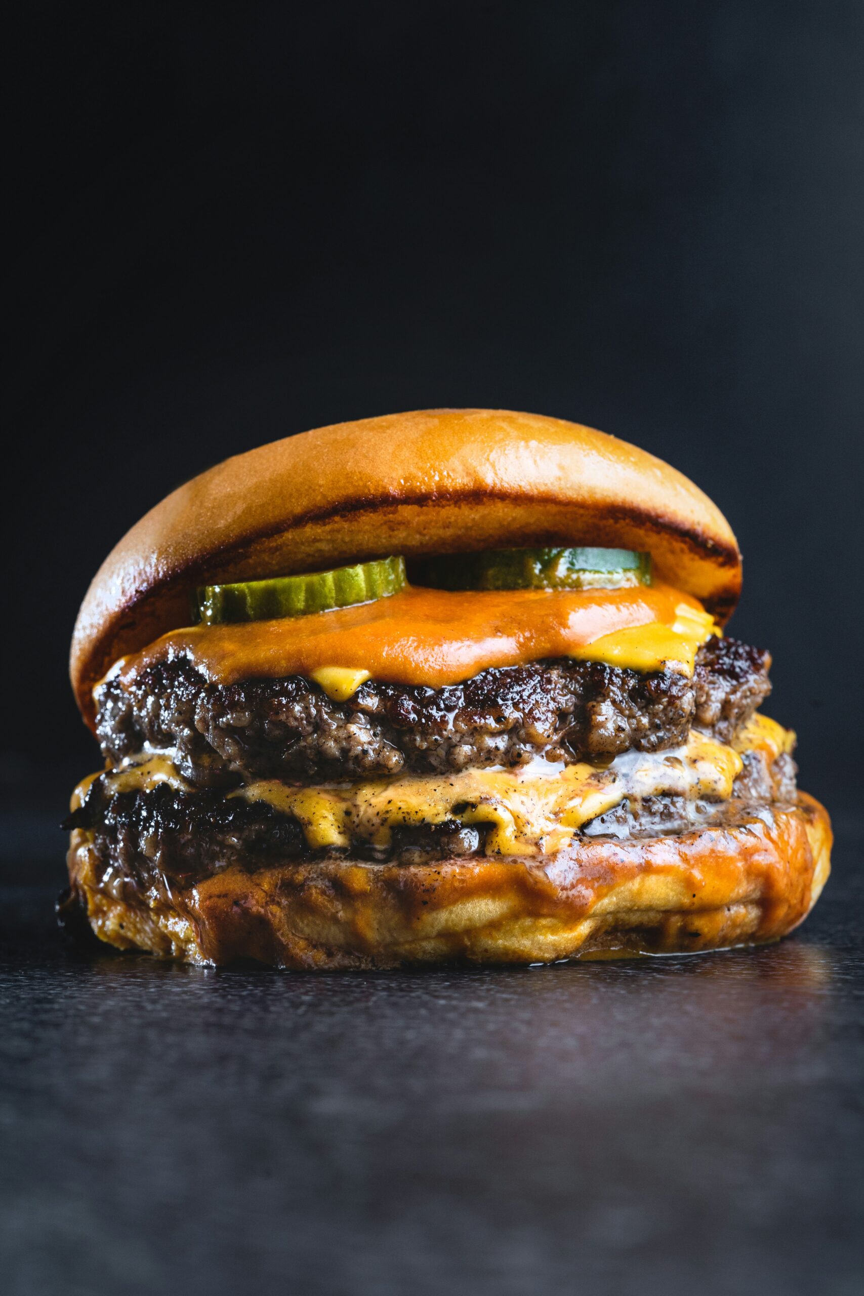 Sizzling cheddar cheese smash burgers on griddle plate surface showing crispy lacy edges