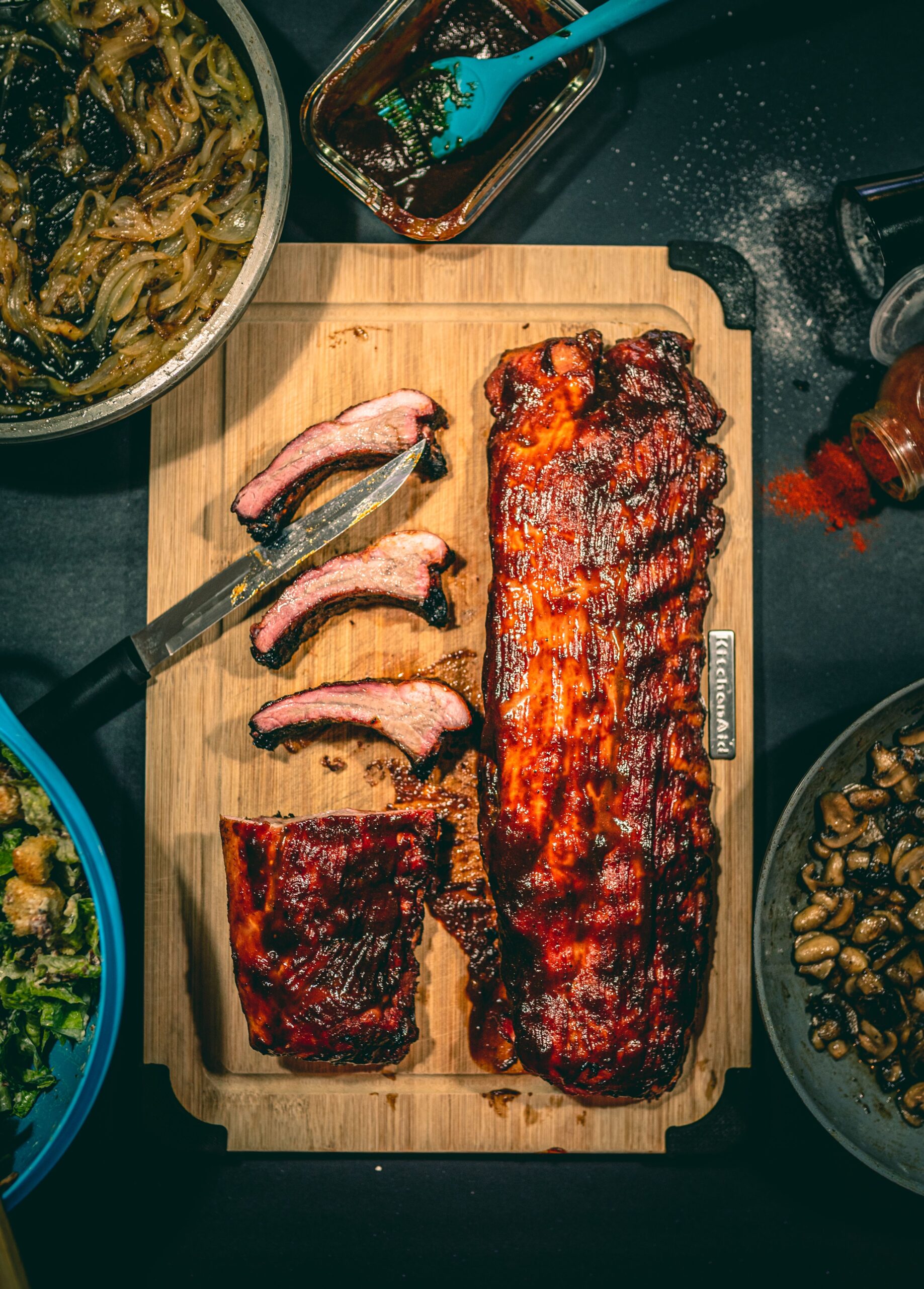 Finished baby back ribs on a gas grill with BBQ glaze on a wooden cutting board from a Lion smoker box recipe