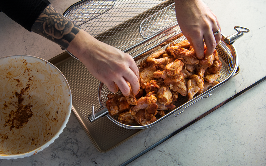 Loading seasoned chicken wings into a Napoleon stainless steel rotisserie basket